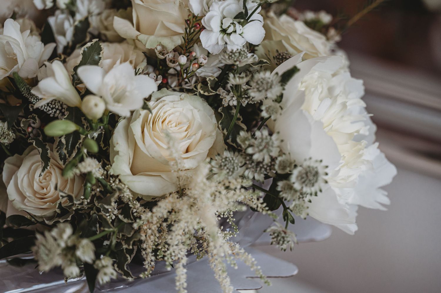 An elegant white and cream wedding bouquet with roses and baby's breath in soft focus.