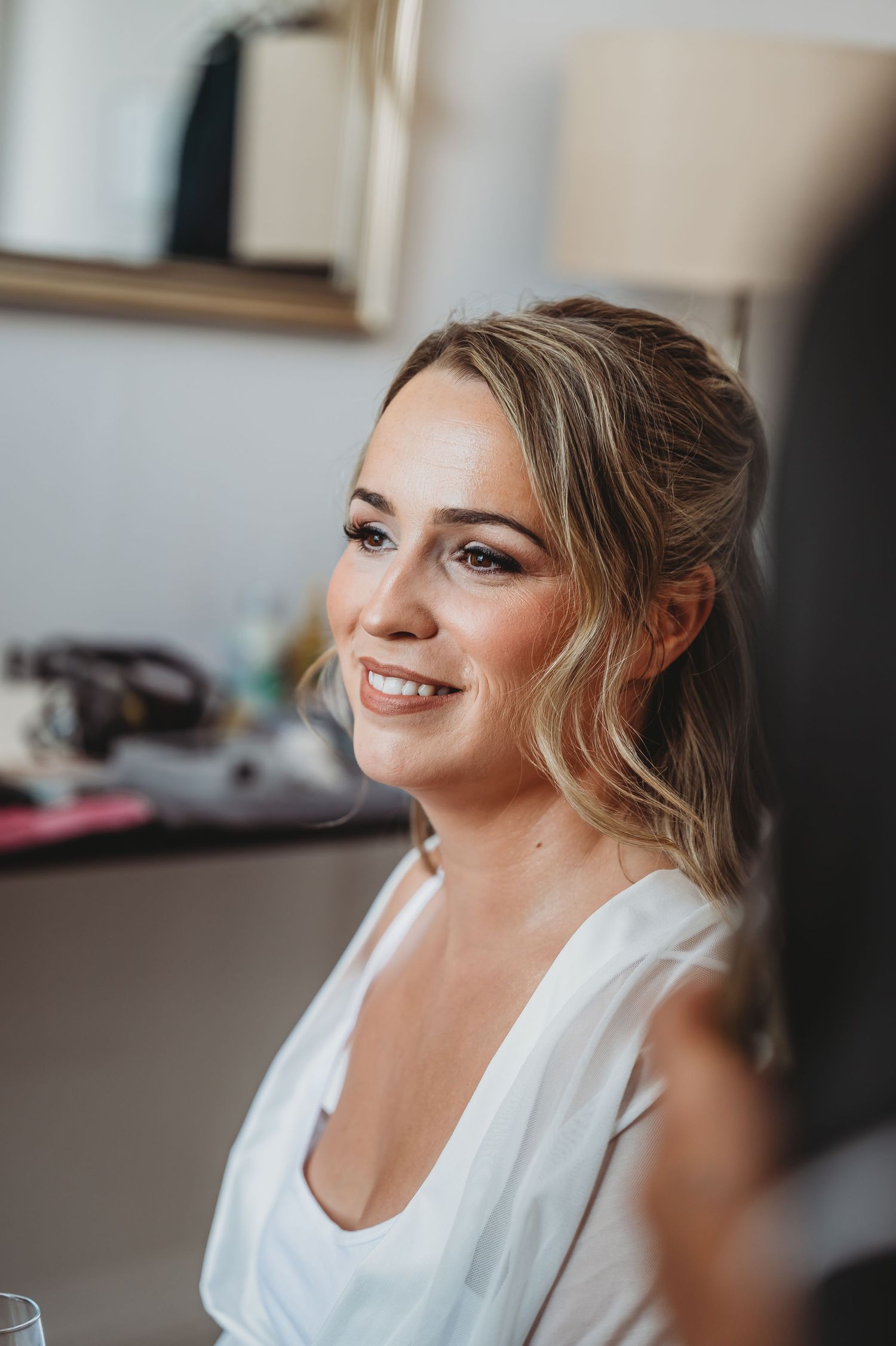 A glowing side profile of someone getting ready for a wedding with natural makeup and blonde wavy hair.