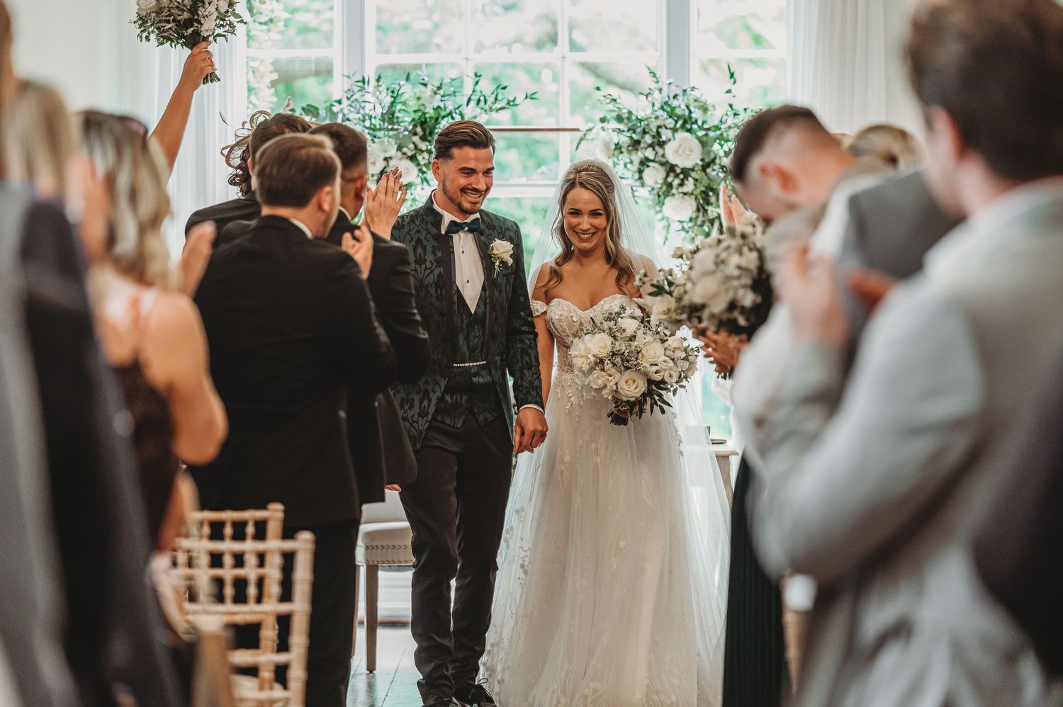 Indoor wedding ceremony with guests standing along both sides of aisle.