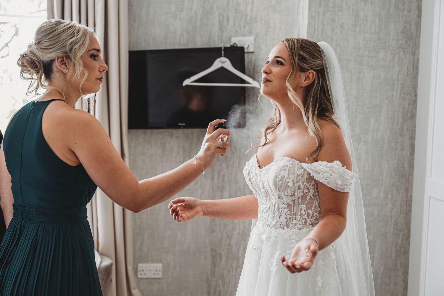 Final wedding dress preparations with bridesmaid helping in modern dressing room.