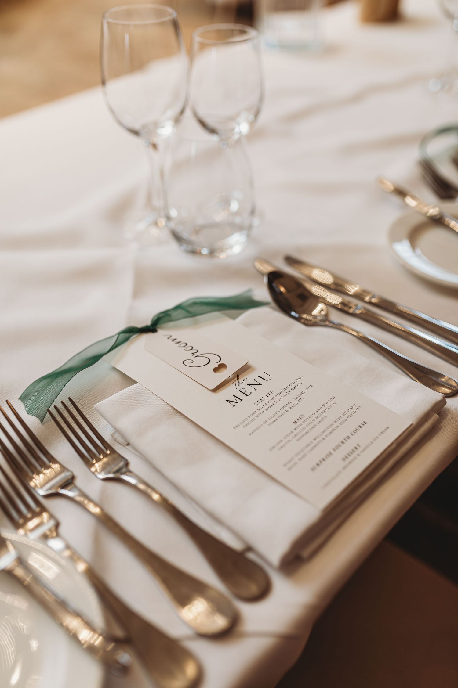 An elegant place setting with menu card, wine glasses and silverware on a white tablecloth.