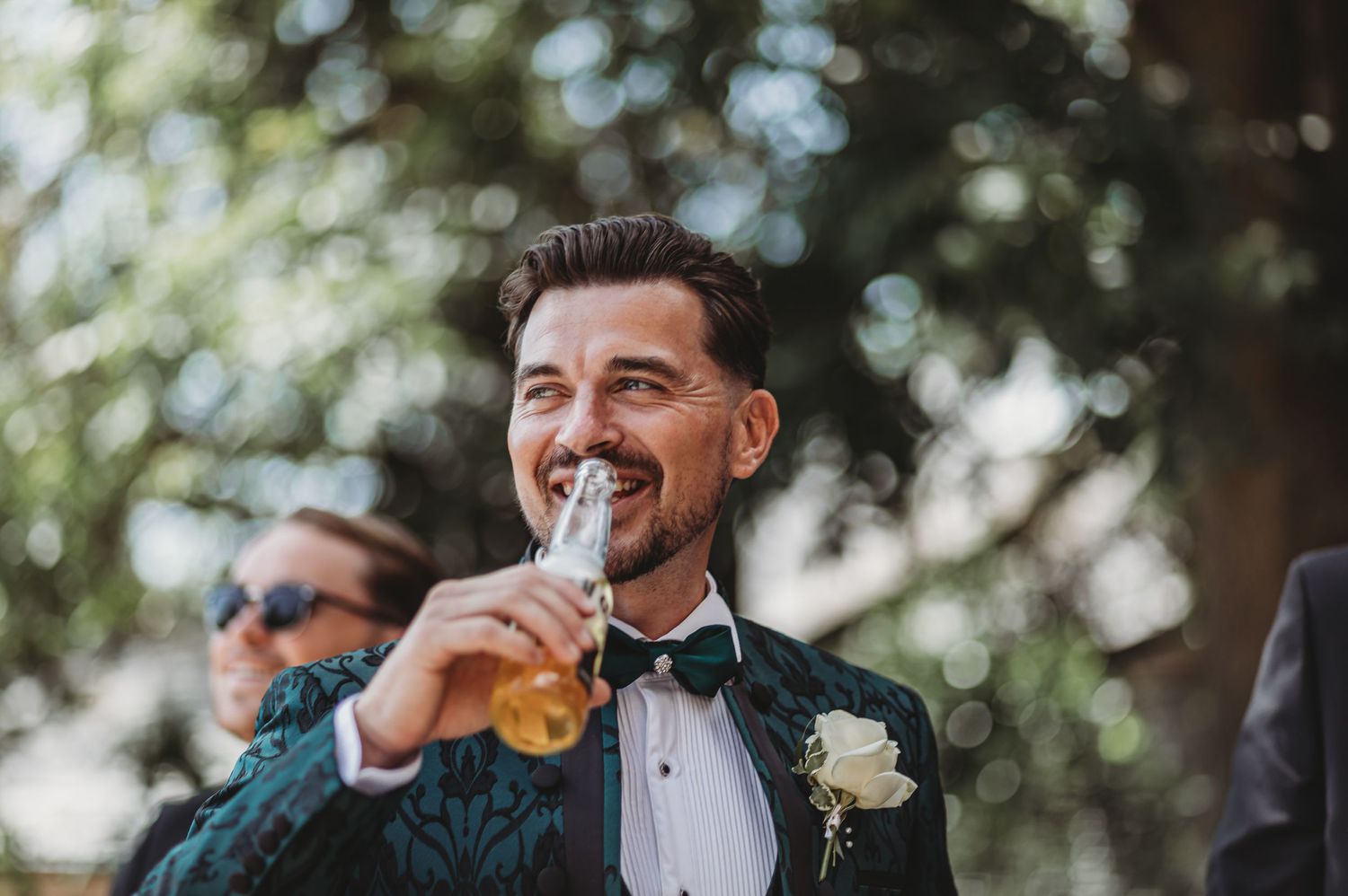 A person in a tuxedo enjoying a drink outdoors during a formal event.