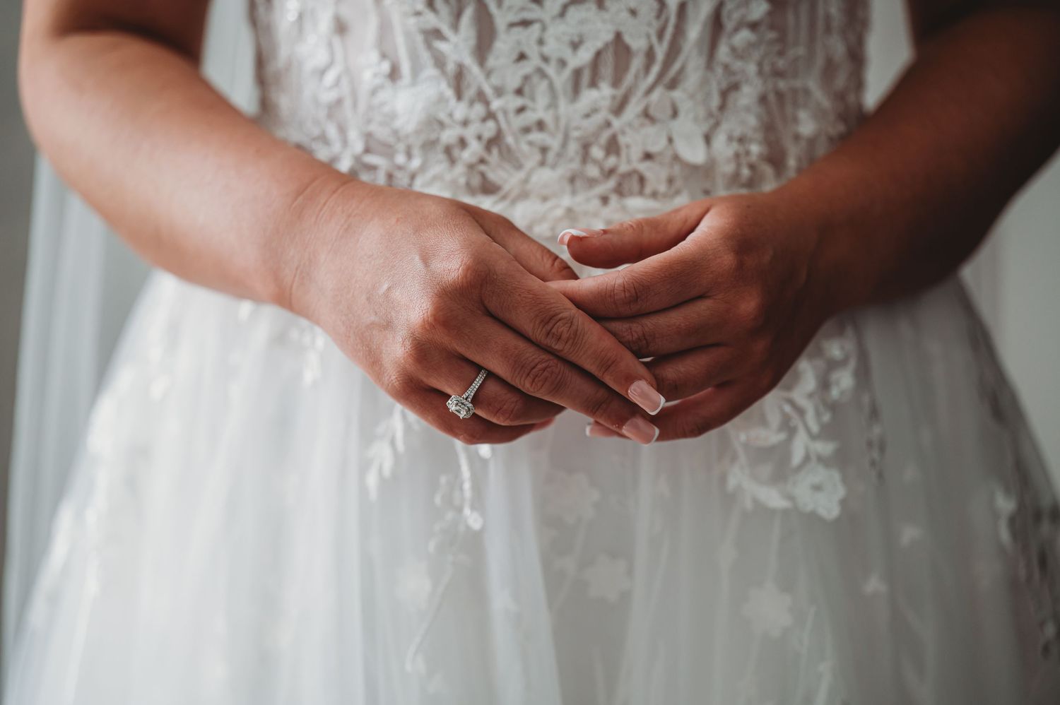 Close-up of bride's hands showing wedding ring and lace dress detail.