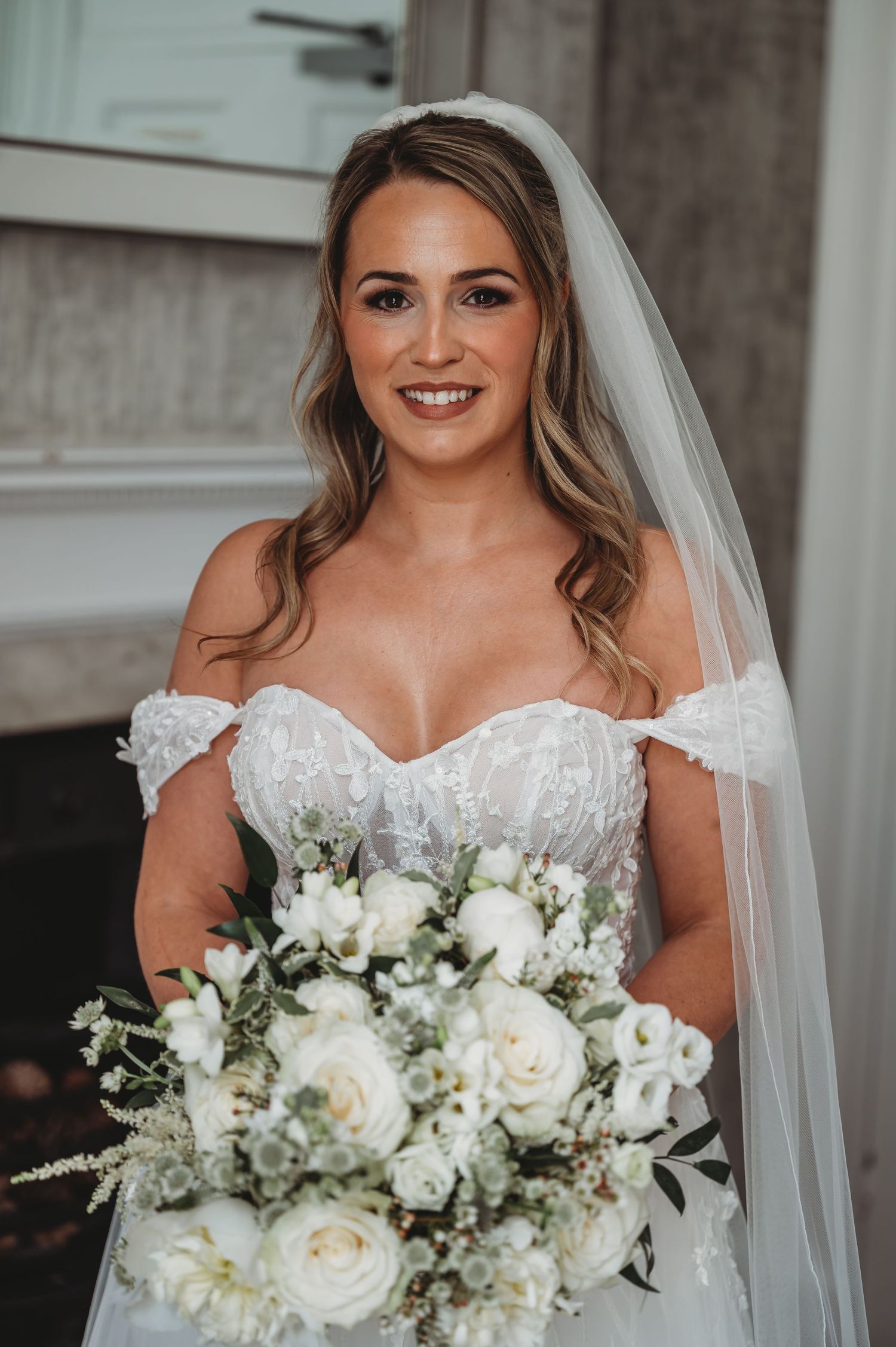 Close-up portrait of bride with white rose bouquet in off-shoulder wedding gown.