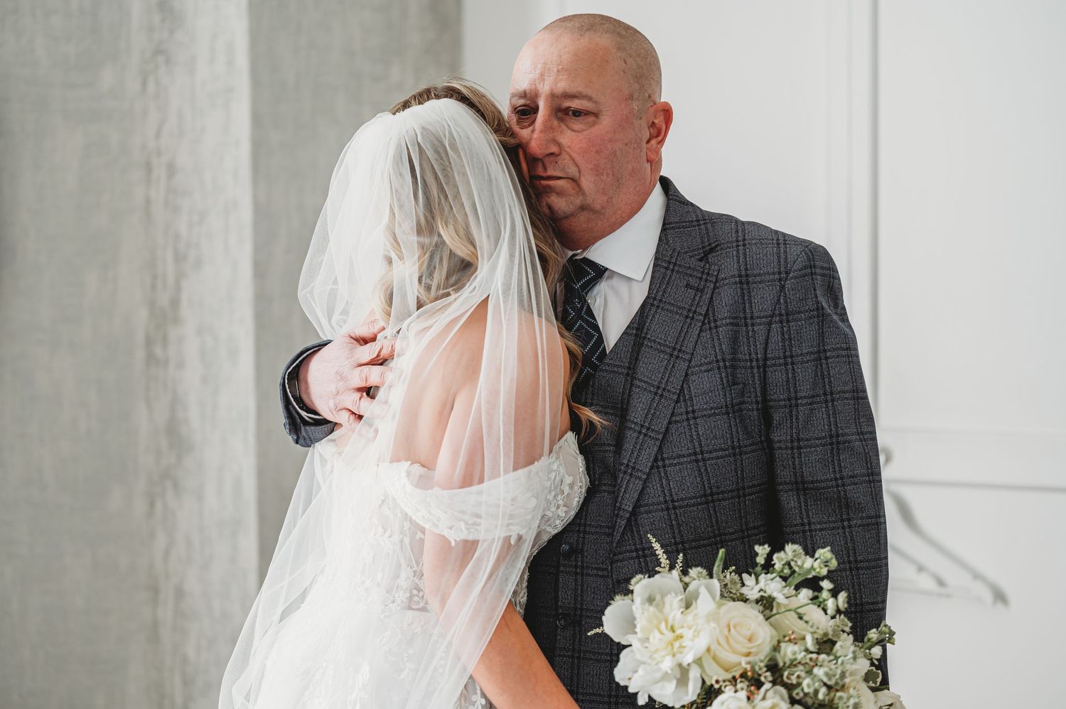 Emotional moment between bride in white dress and suited man during wedding ceremony.