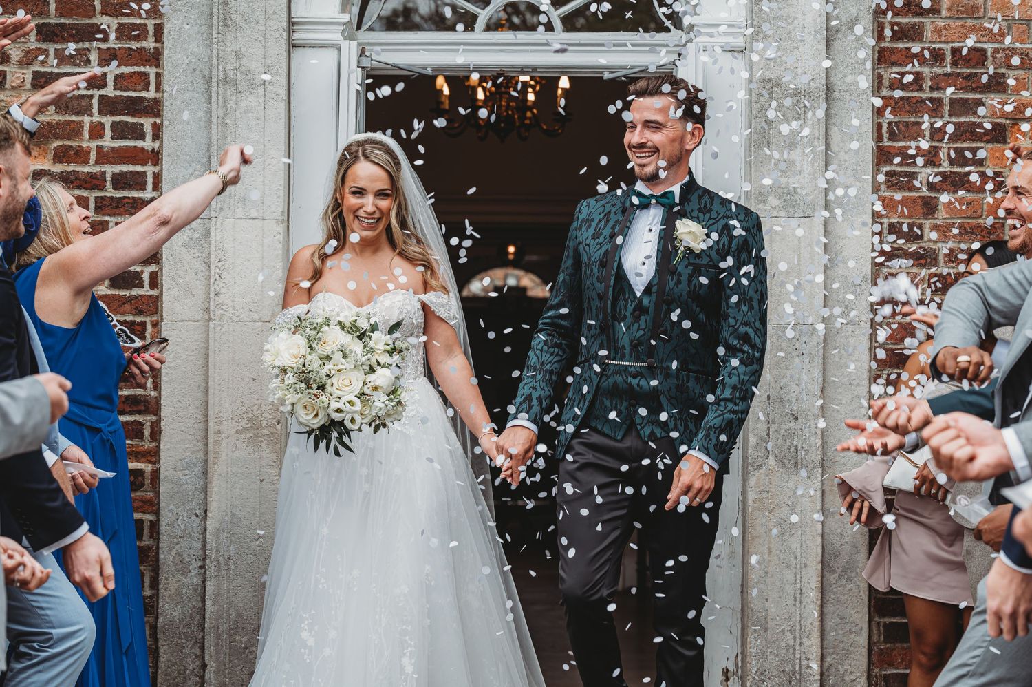 Celebratory wedding exit with guests throwing confetti outside brick church entrance.