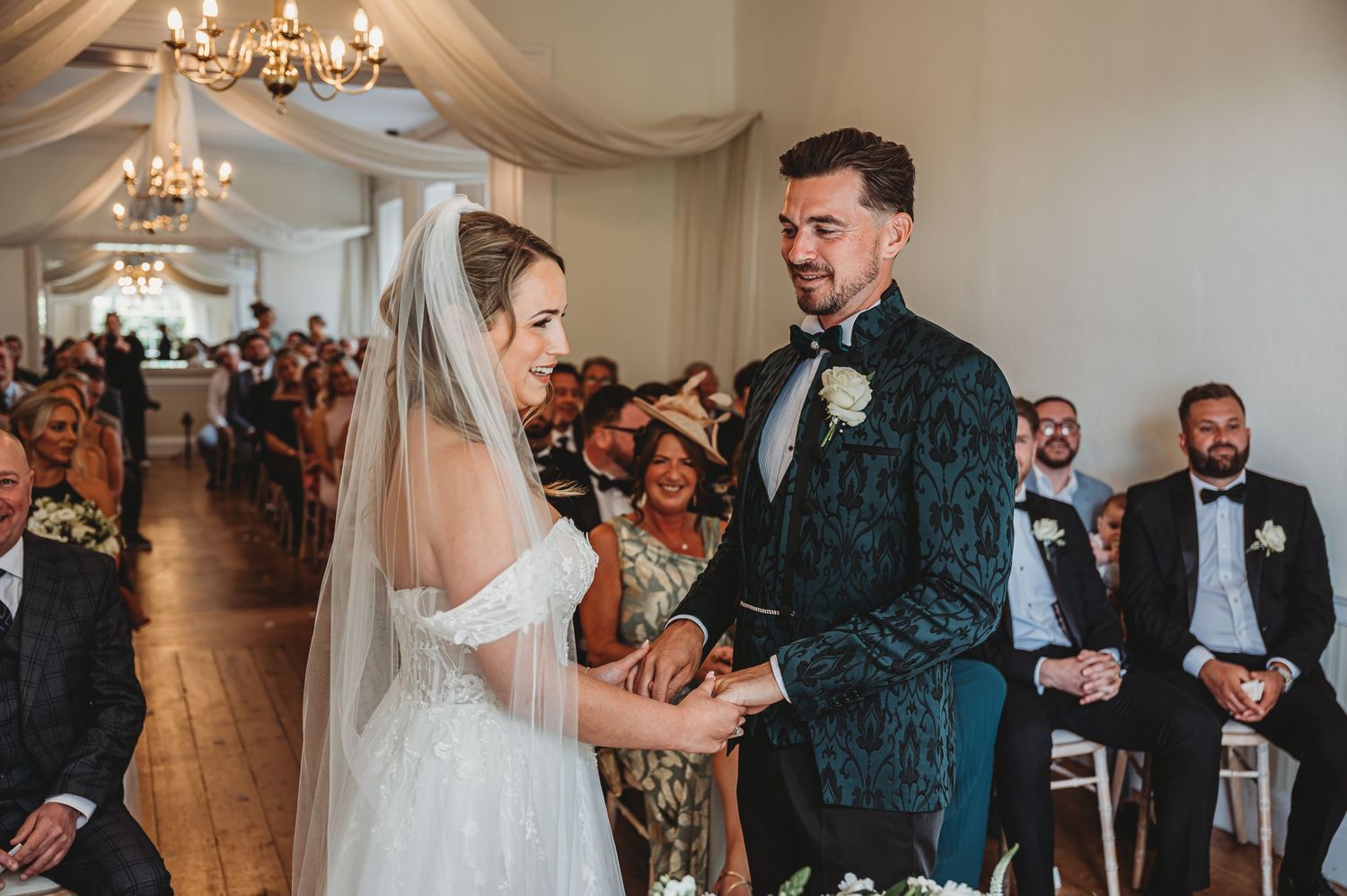 Emotional wedding ceremony moment in elegant white room with chandelier and draped fabric.