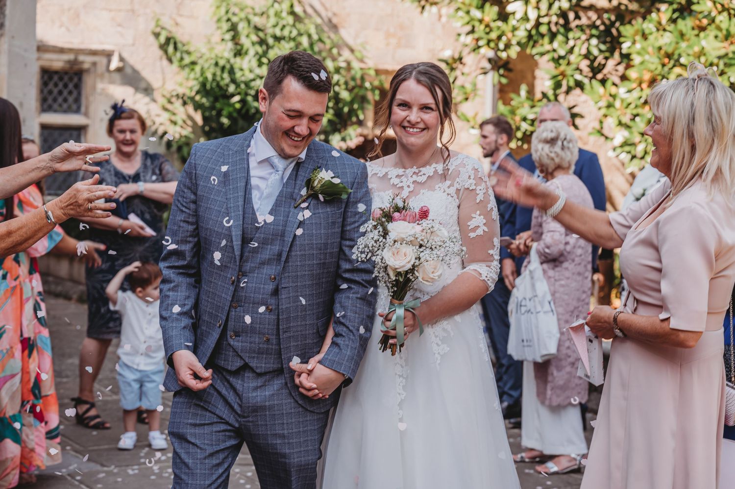 A joyful couple exit their wedding ceremony while guests throw confetti in celebration at an outdoor venue.