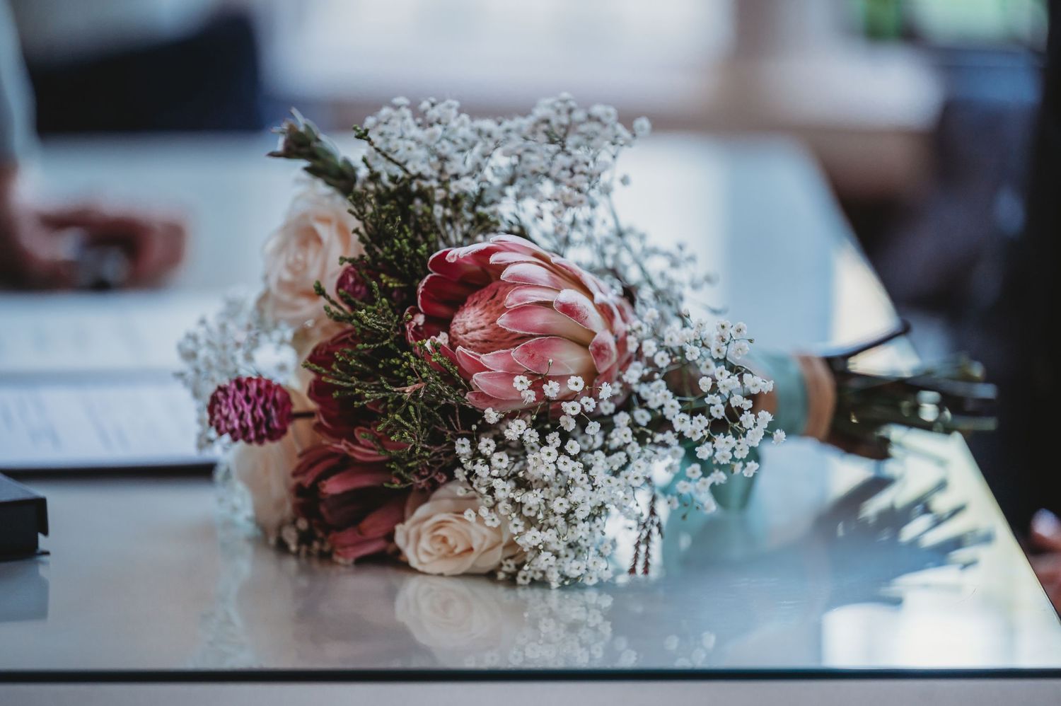 A delicate bouquet of pink roses and baby's breath flowers arranged on a reflective surface in soft lighting.