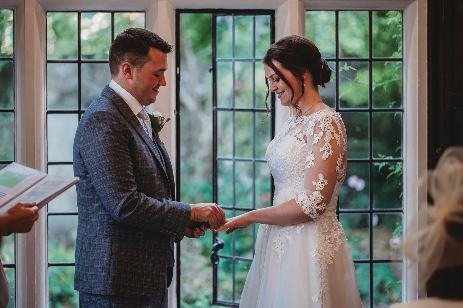 A couple exchanges vows during their wedding ceremony in front of large windows with natural light streaming in.