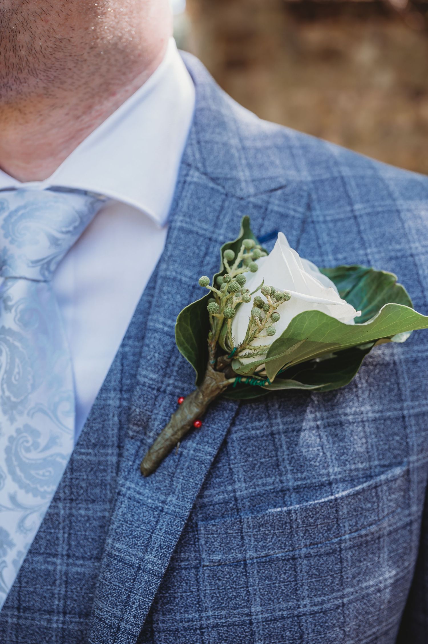 Close-up view of a white floral boutonnière with greenery pinned to a blue plaid suit jacket lapel.