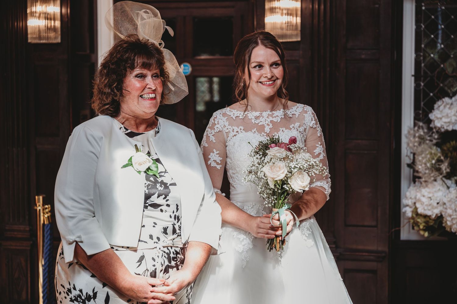 Two people in elegant white attire pose together at a wedding celebration with floral bouquets.