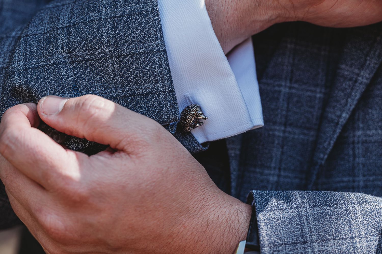 Close-up of hands adjusting a gray plaid suit sleeve with a silver cufflink detail.