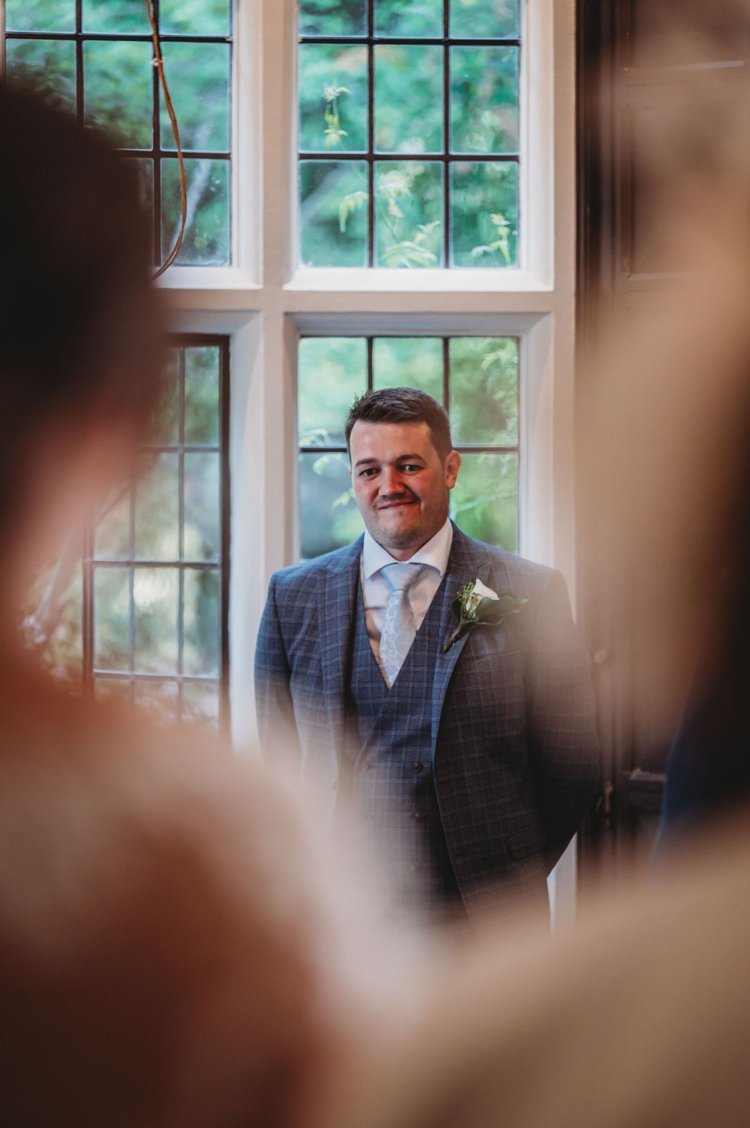 A wedding scene shows a suited person standing by a bright window with blurred figures in the foreground.