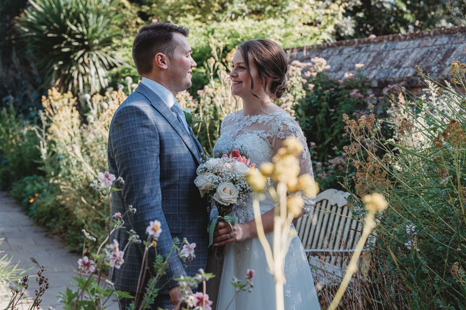 Two newlyweds sharing a romantic moment in a lush garden setting with soft sunlight and vintage decor.