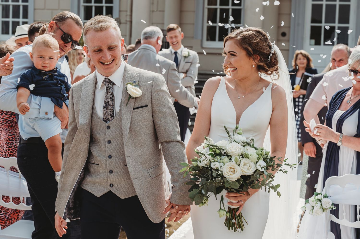 A celebratory wedding exit moment with guests throwing confetti outside a stone building.