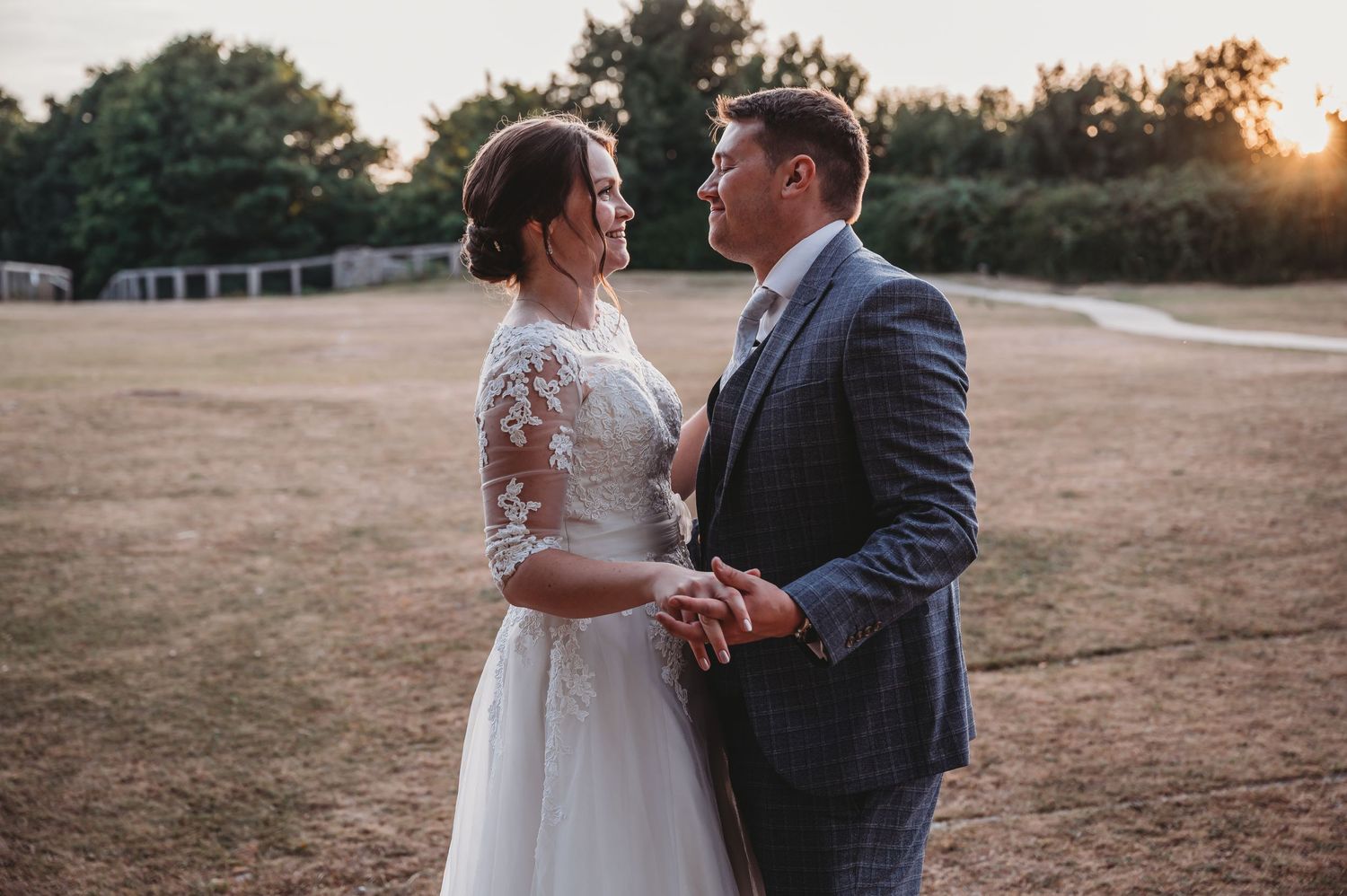 A couple shares an intimate moment at sunset, the bride wearing a lace sleeve gown and groom in a gray suit.