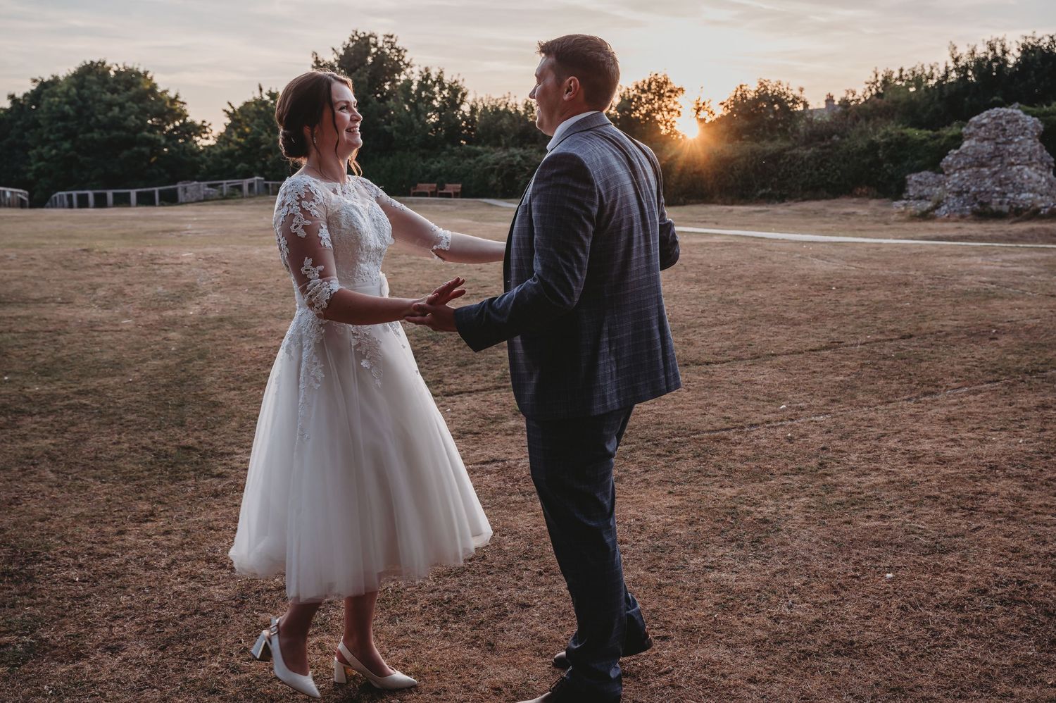 Couple shares a romantic moment in their wedding attire at golden hour in a rustic outdoor setting.