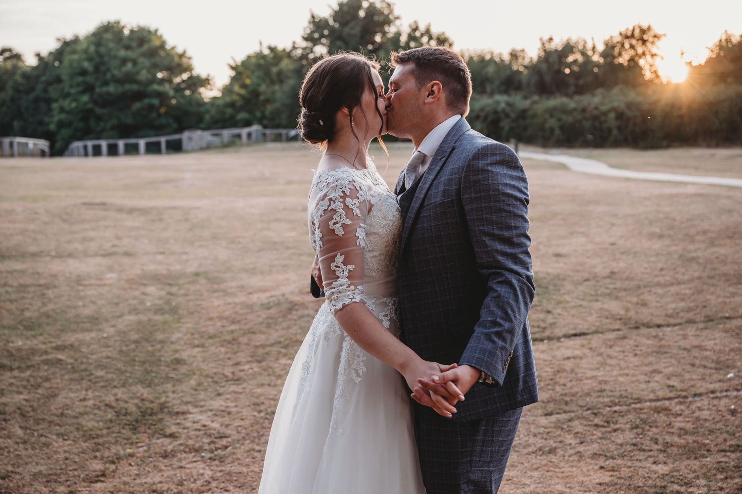A romantic sunset wedding photo of a couple sharing an intimate moment in a rustic outdoor setting.