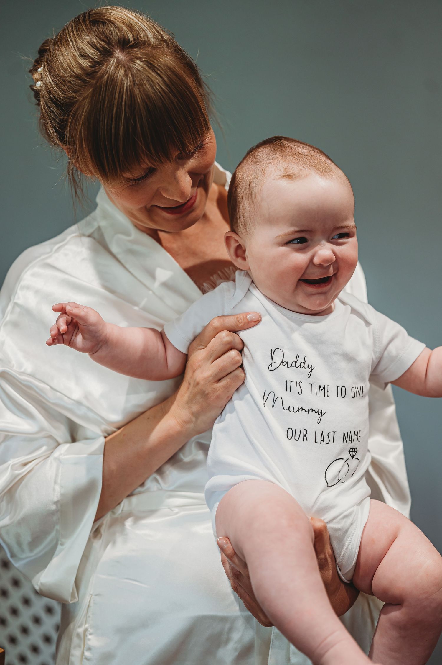 Sweet candid moment showing a parent in a white shirt sharing a laugh with a smiling baby wearing a message onesie.