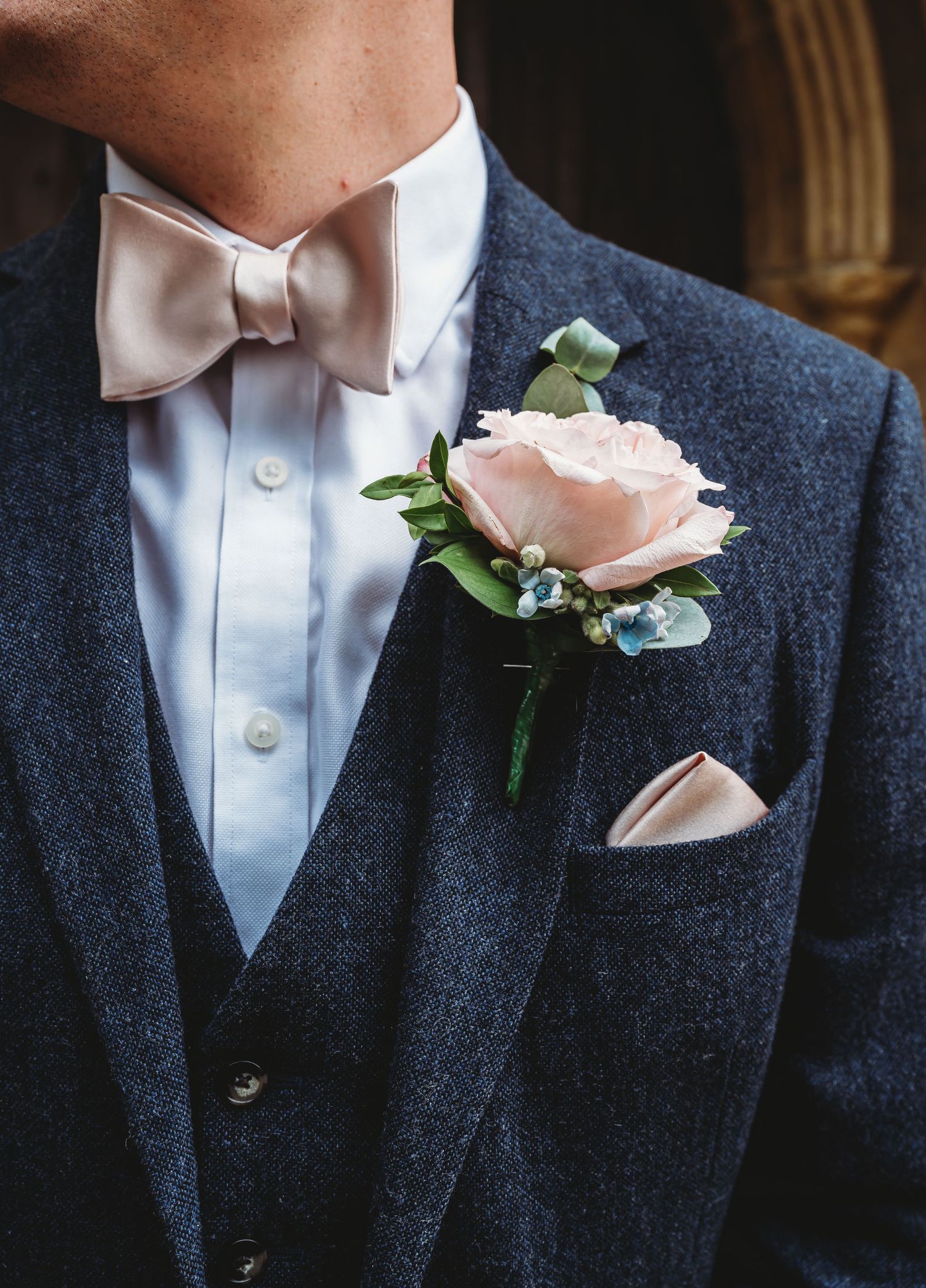 A light pink rose boutonniere adorns a navy blue suit with pink bow tie and matching pocket square.