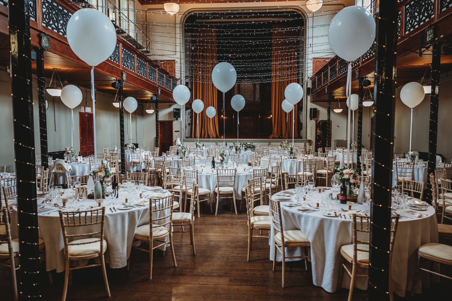 Elegant wedding reception venue with white balloons and tables set in a historic ballroom with ornate architectural details.