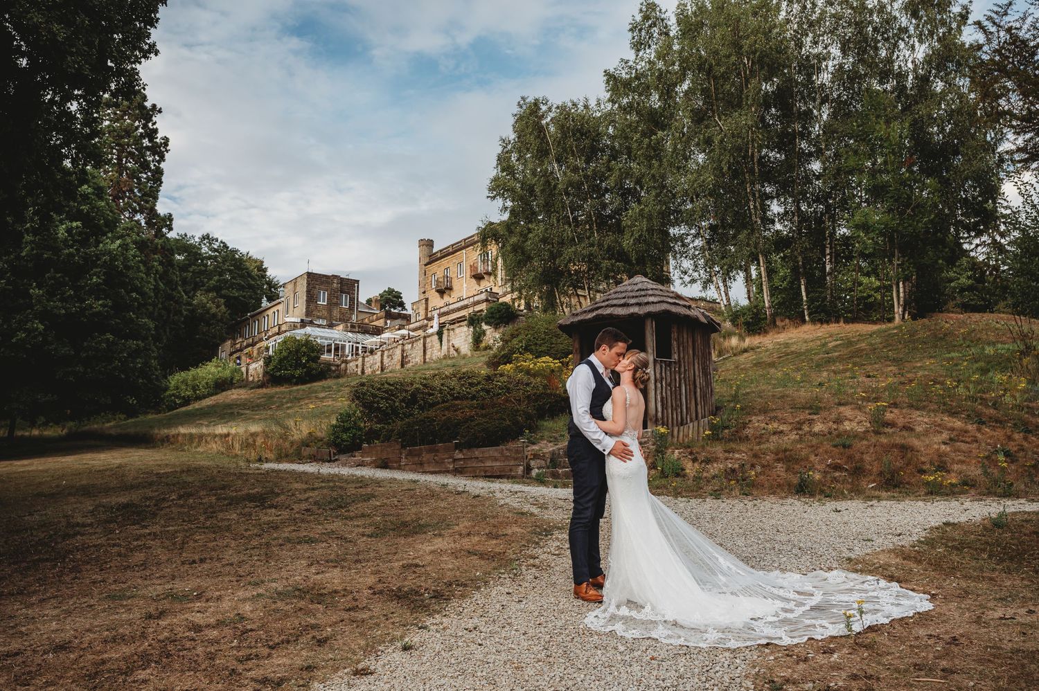 A scenic outdoor wedding scene on a rustic property with a romantic moment captured near a wooden shelter.