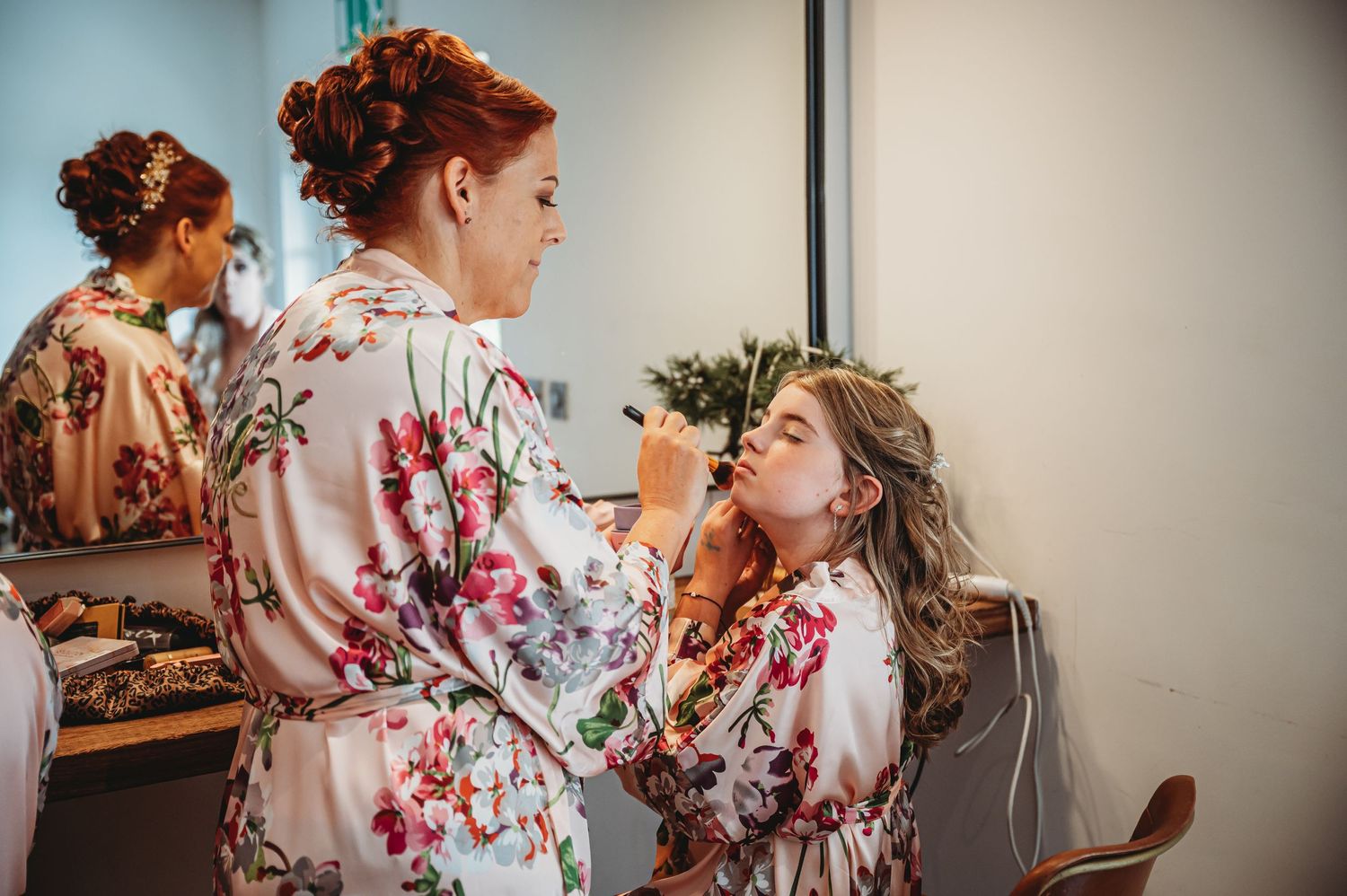 Makeup artist applies cosmetics to someone wearing a floral robe during wedding preparations.