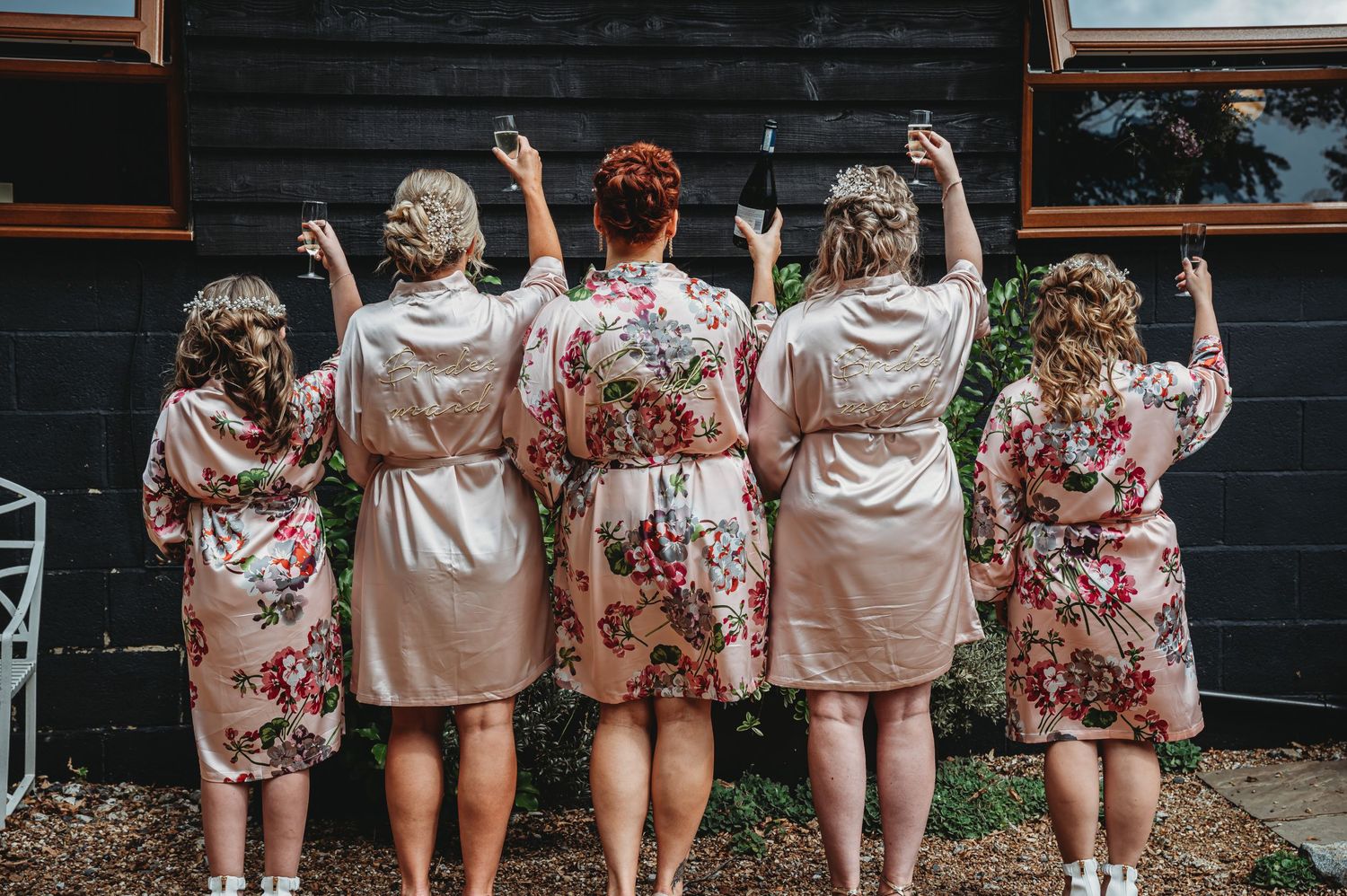 A group in matching floral silk robes raise their hands in celebration while facing a dark wooden wall.