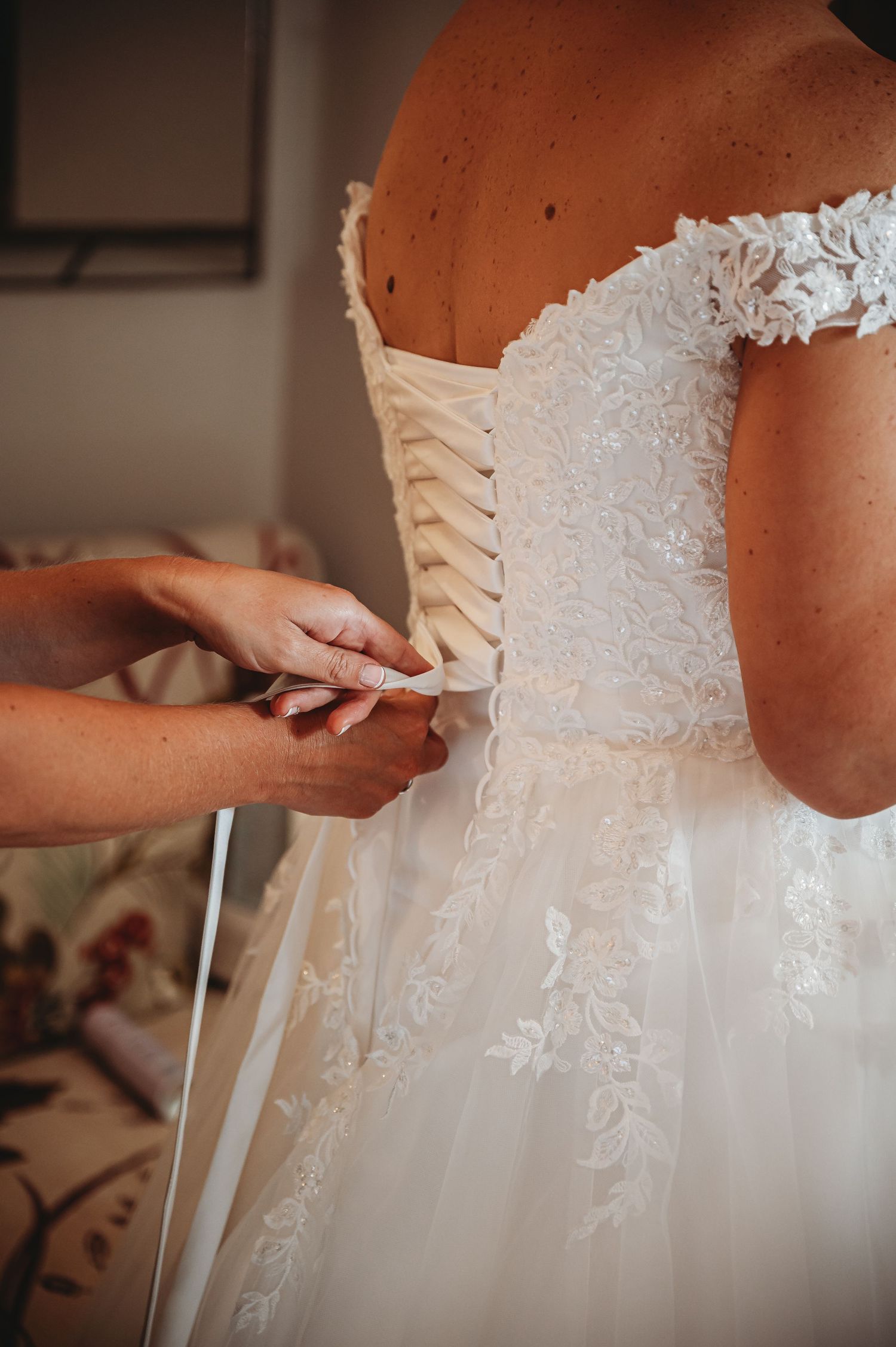 Hands lacing up the back of an ornate white lace wedding dress with corset-style closure.