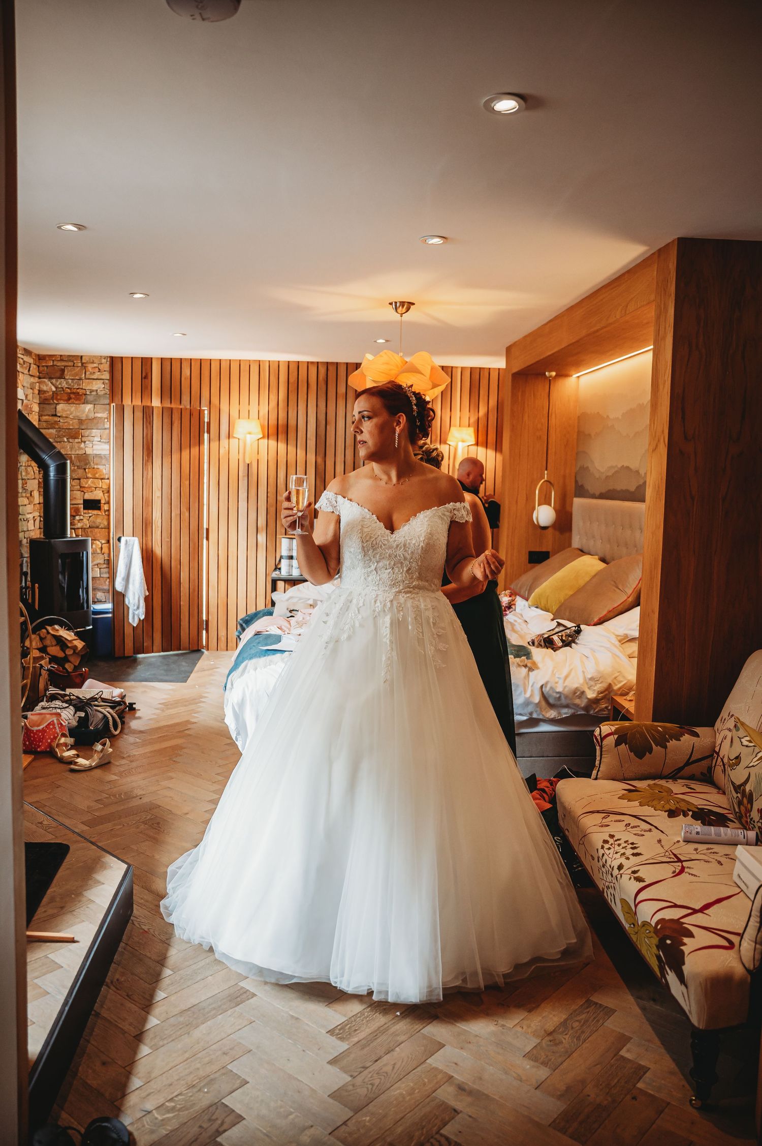 A beautiful white ball gown wedding dress with off-shoulder detail and tulle skirt being fitted in a warm-lit dressing room.