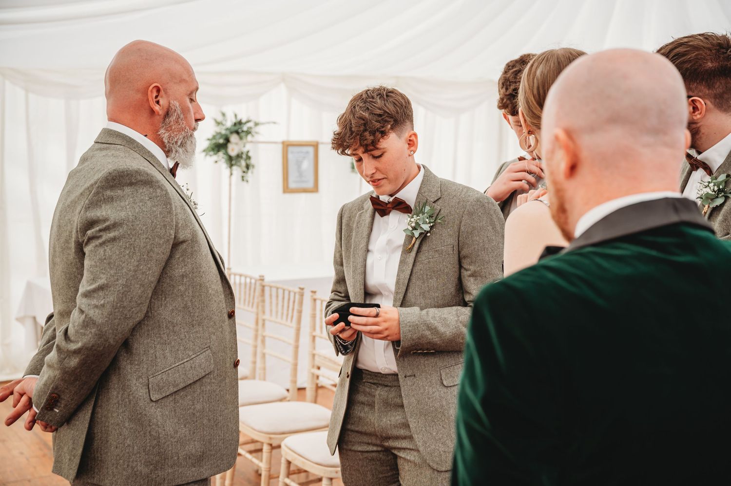 A small group gathers in formal attire at an indoor event, with grey suits and bow ties visible in the scene.