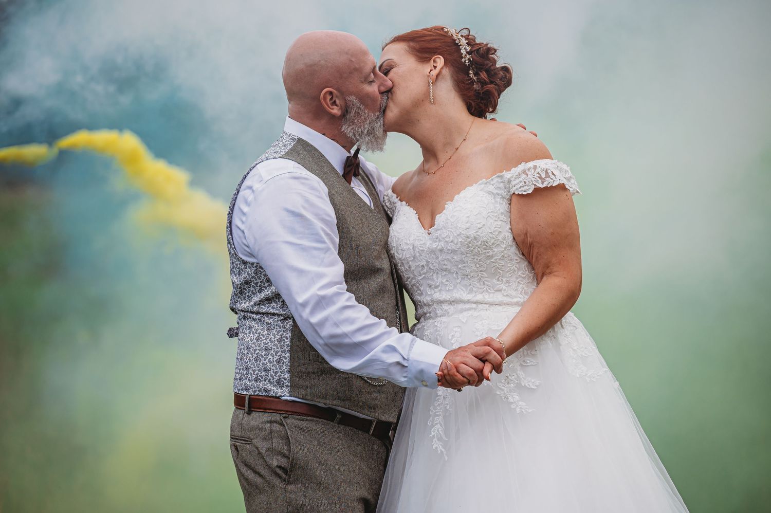 A romantic wedding photo with colorful smoke bomb effect creating a dreamy teal and yellow atmosphere in the background.