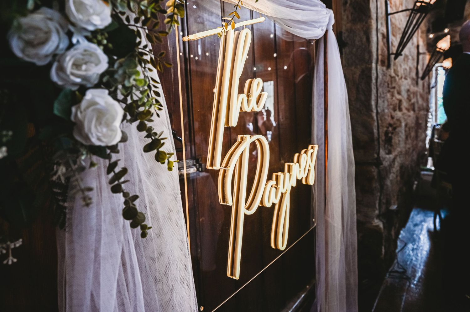 An illuminated neon "I Do" sign glows between white fabric draping and floral decorations at a wedding venue.
