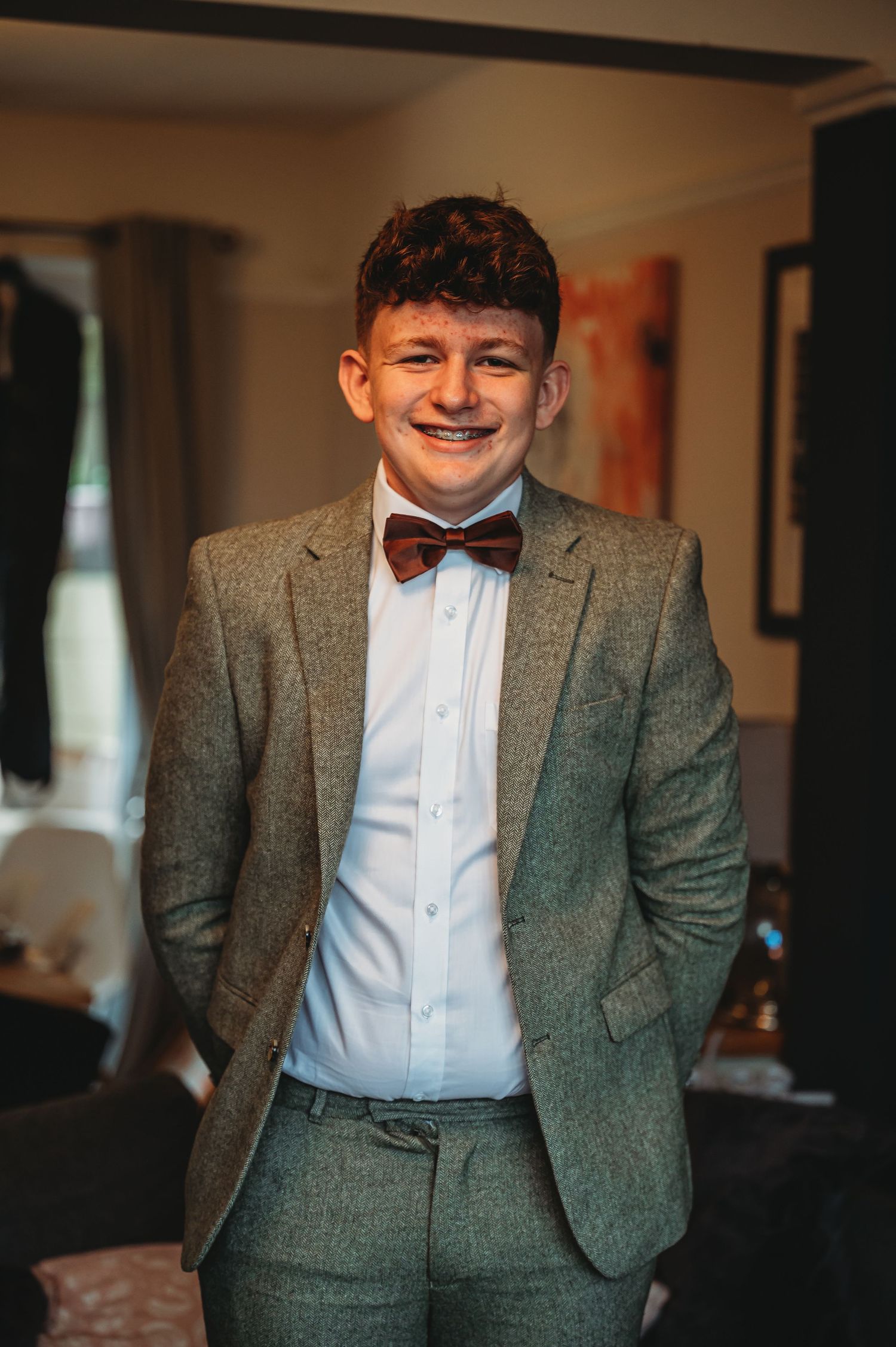 A person wearing a gray suit and brown bow tie stands smiling in an indoor setting.
