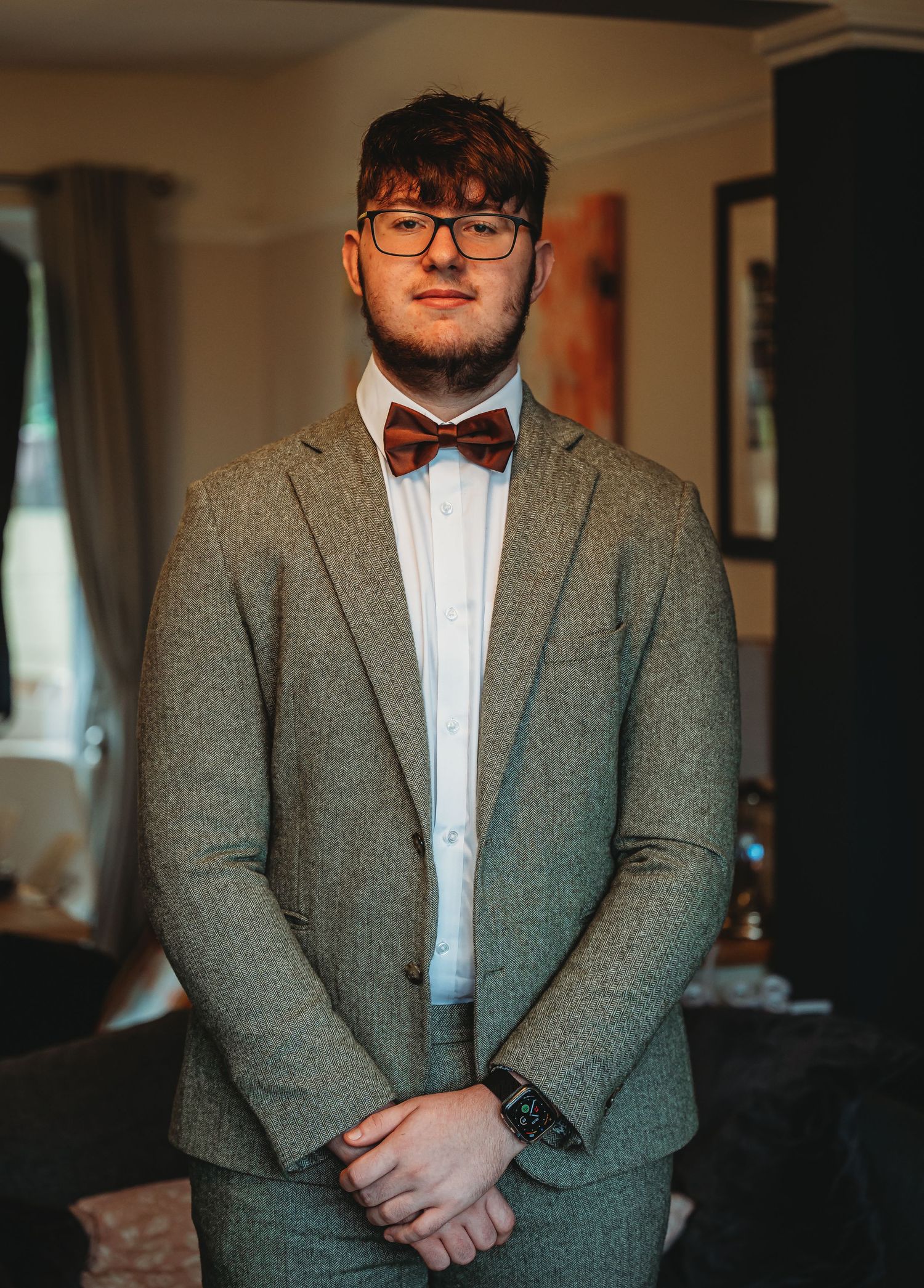 A dapper look featuring a grey tweed blazer, white dress shirt, and burgundy bow tie in an indoor setting.