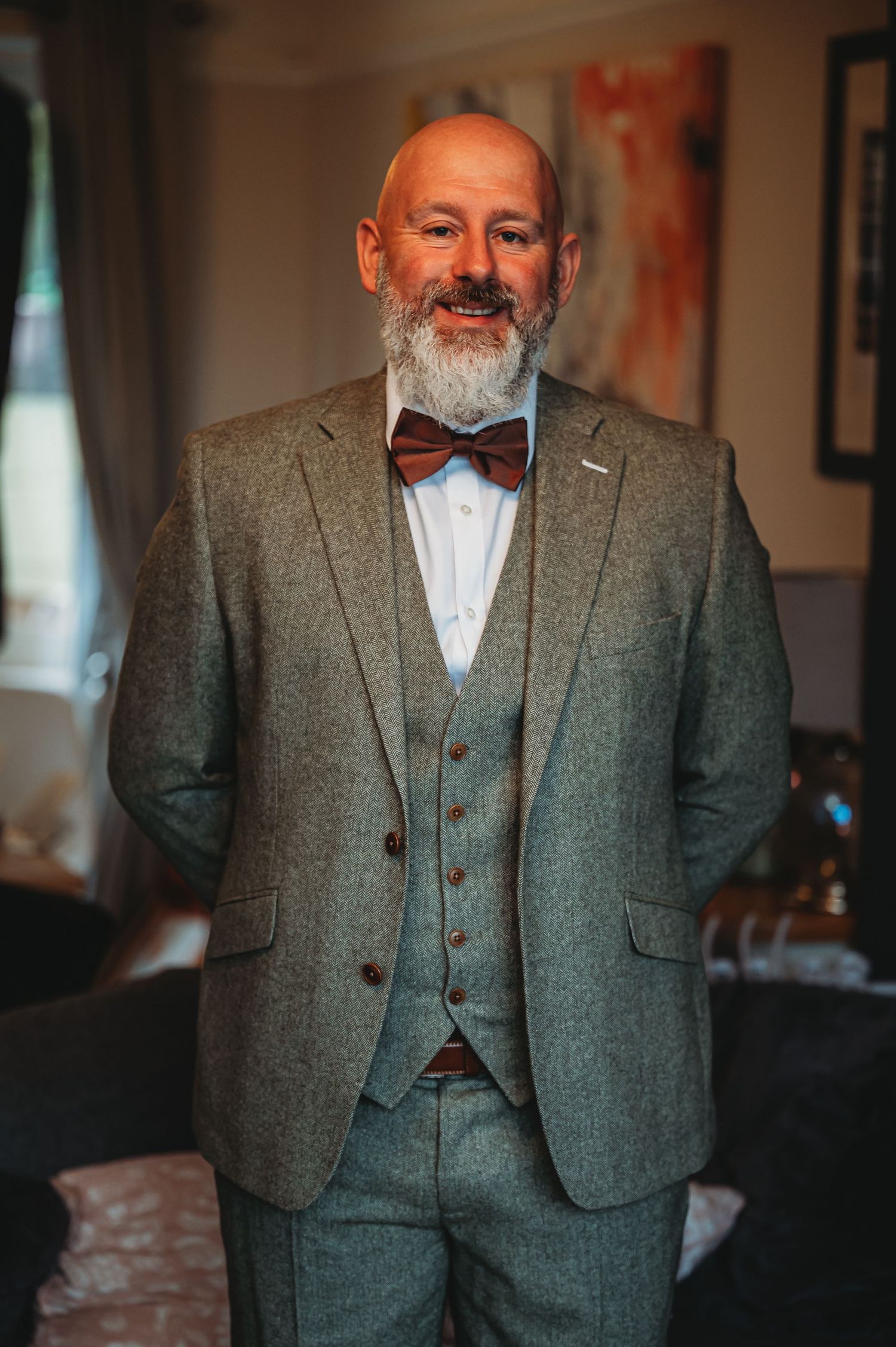 Gentleman in a dapper grey three-piece suit and bow tie smiles warmly in an indoor setting.