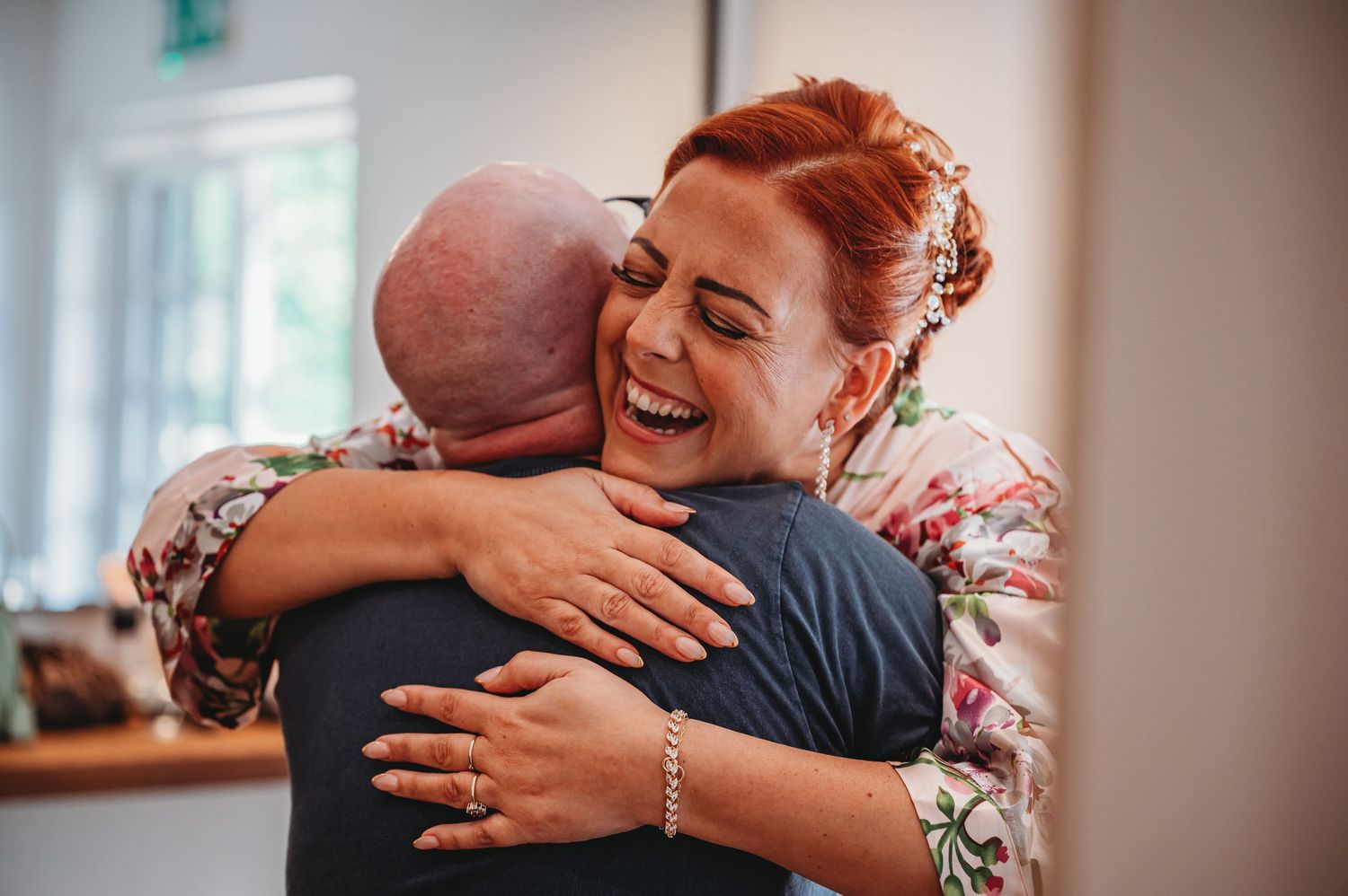 Two people share a joyful embrace and laugh together in a warmly lit room, creating a heartfelt candid moment.