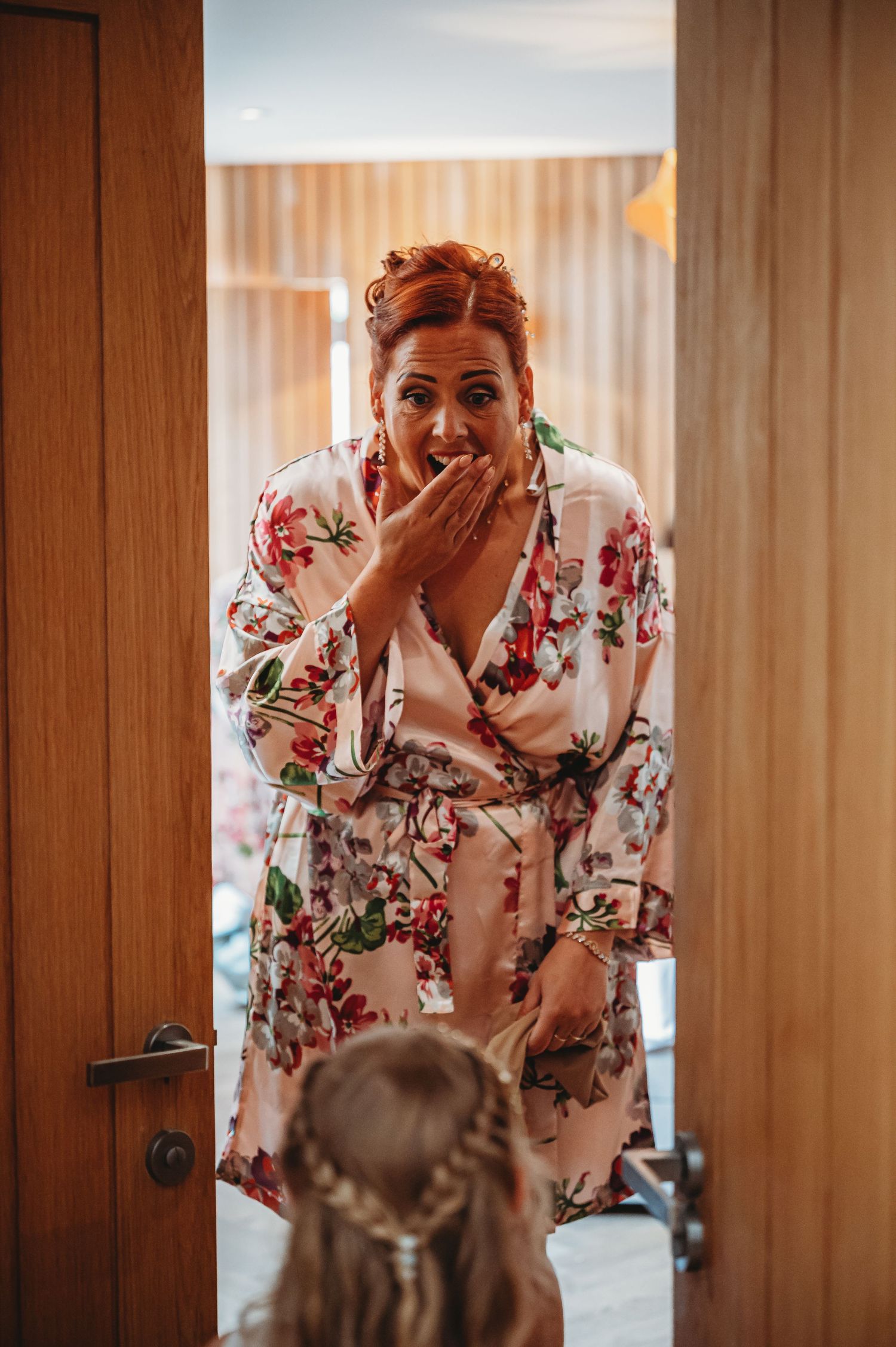 Someone in a floral robe reacts with excitement and covers their mouth while looking down at unseen person.