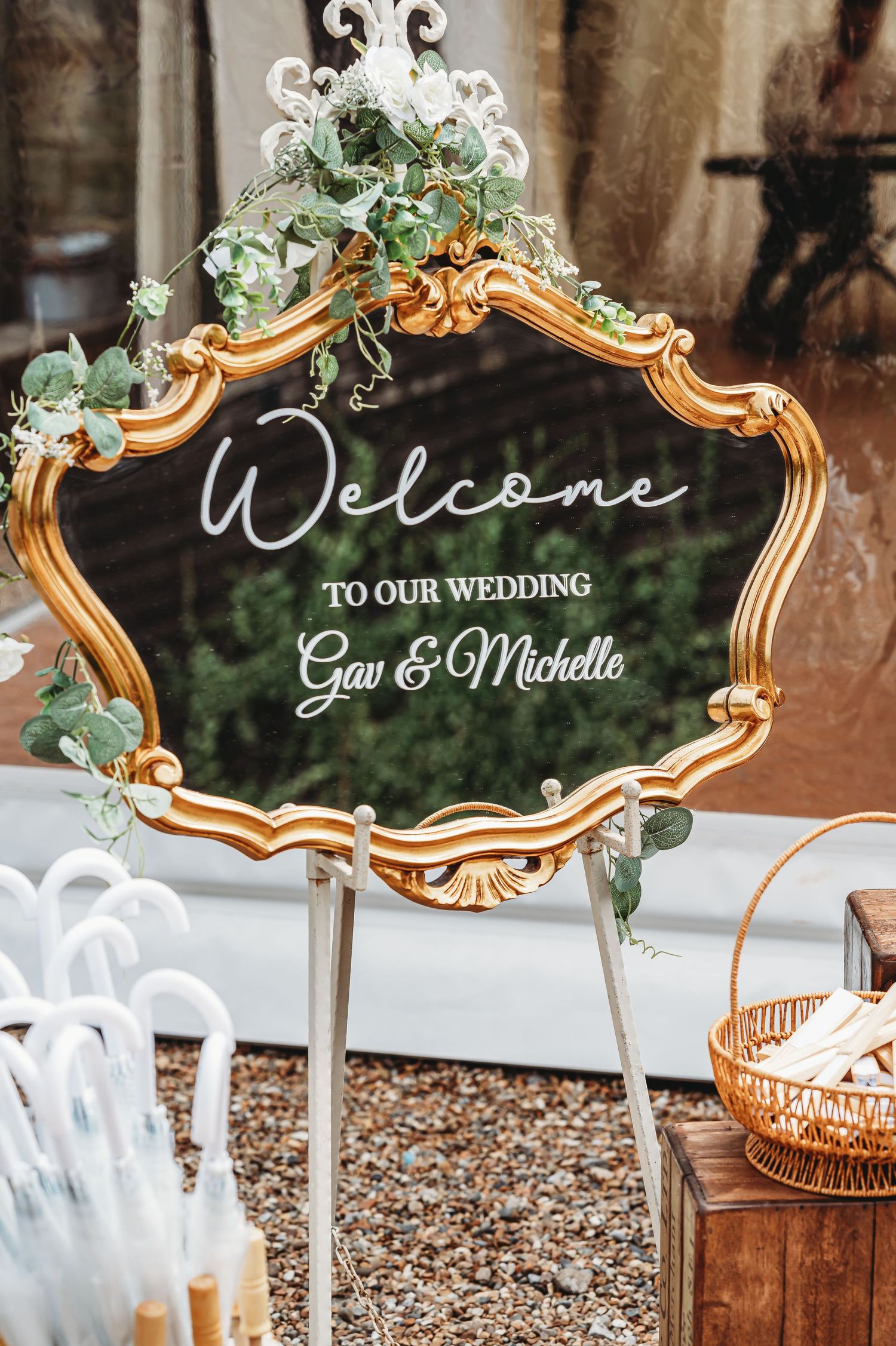 Elegant gold-framed wedding welcome sign with ornate details and eucalyptus greenery decorations on display stand.