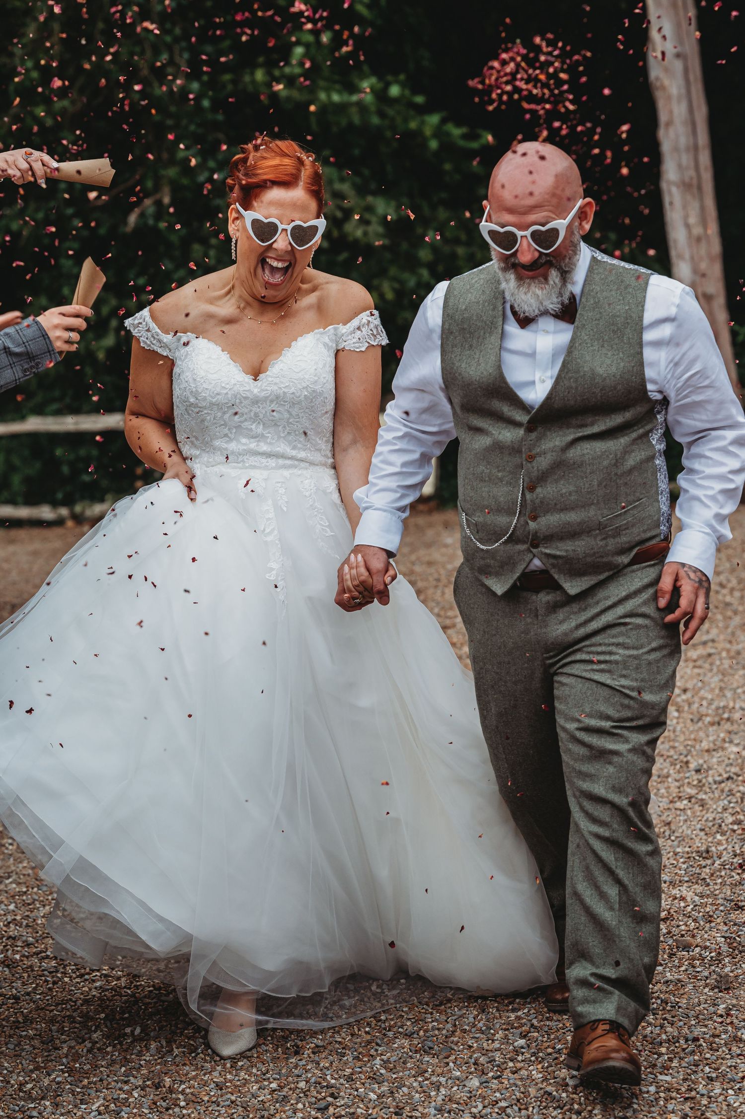 A wedding couple walking hand in hand while confetti falls around them in a casual outdoor forest setting.