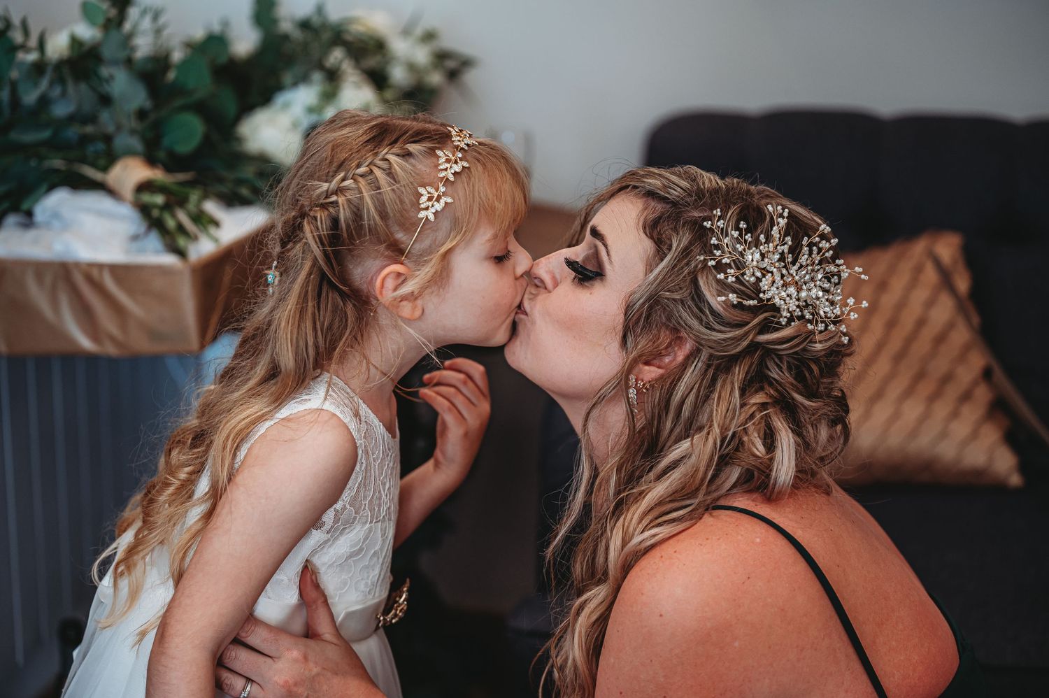 Two people wearing delicate floral headpieces share a tender moment together in a cozy indoor setting.