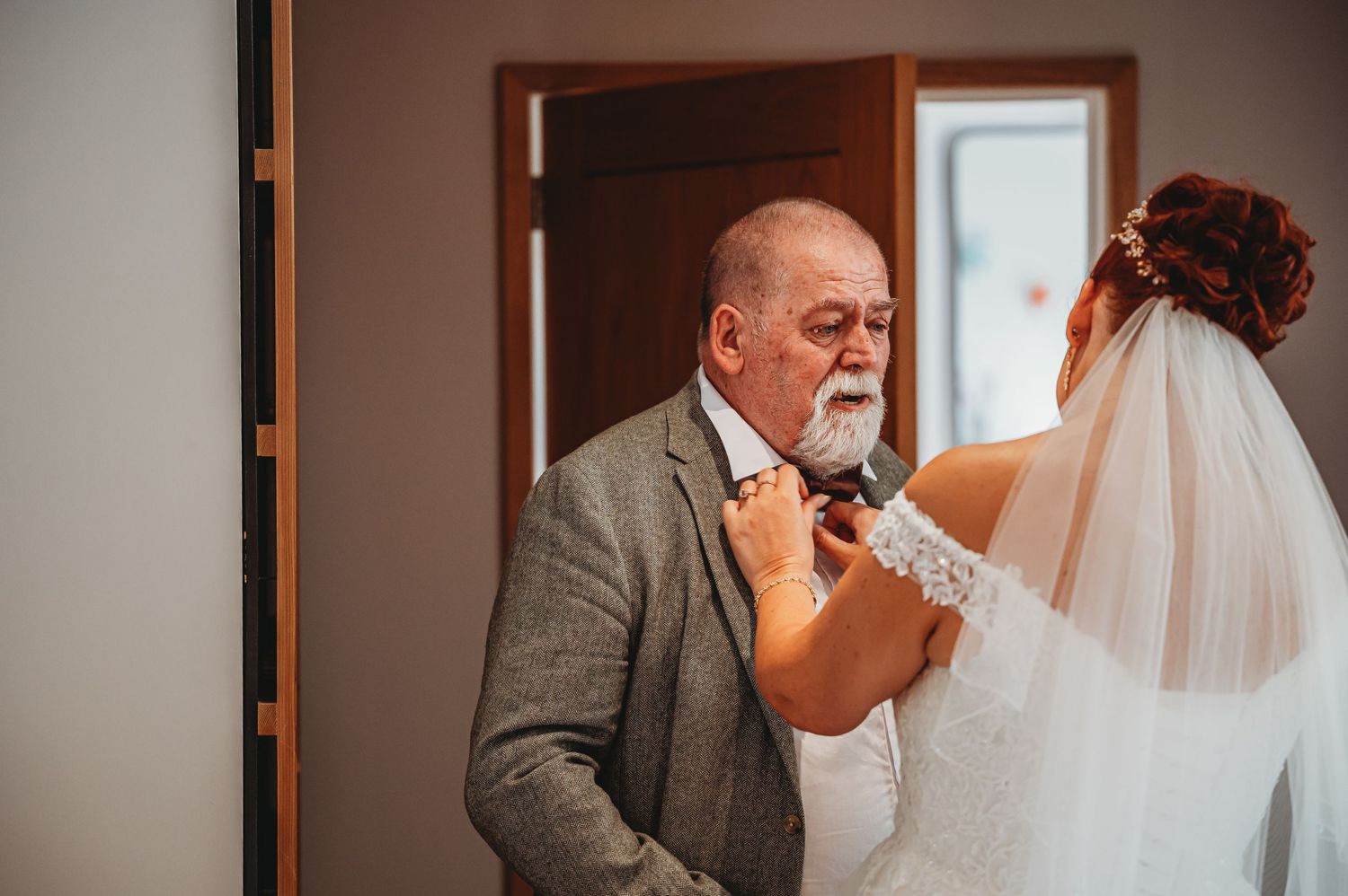 An emotional moment during a wedding as someone wearing a gray suit appears touched while looking at a bride in a veil.