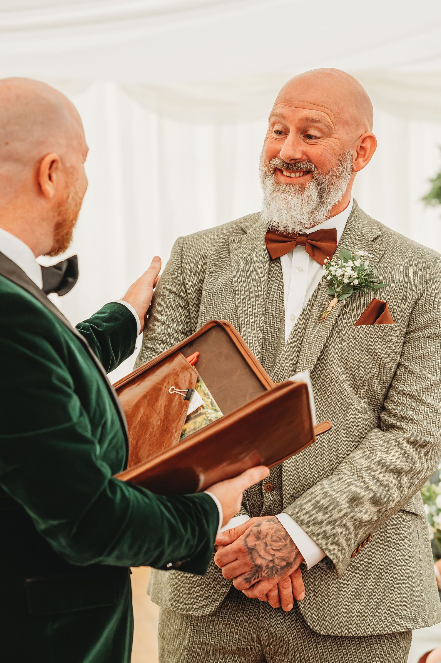 Two people at a wedding ceremony sharing a joyful moment as one reads from a leather-bound book.