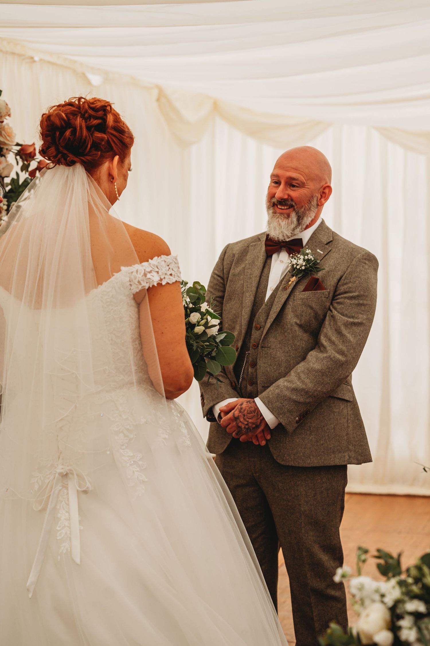 A heartfelt moment during a wedding ceremony as two people exchange vows in an elegant white tent setting.