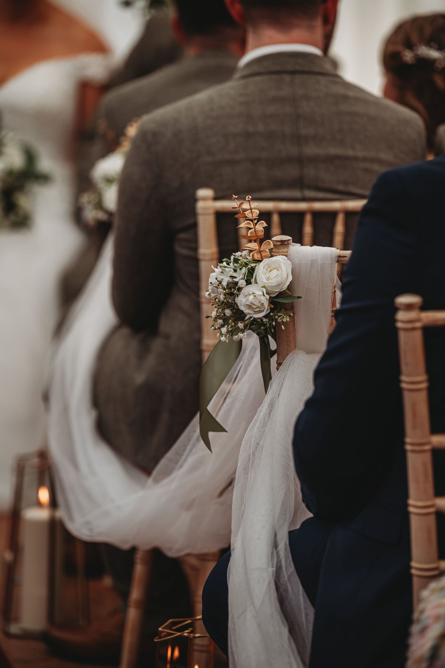 A romantic wedding chair decorated with white roses, delicate tulle fabric and a flowing ribbon at a reception venue.