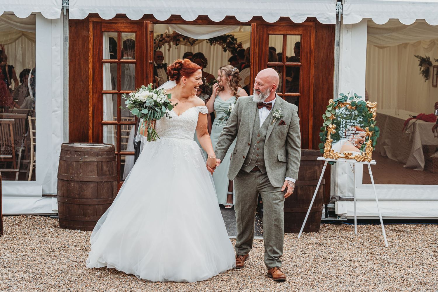 A romantic wedding scene with a couple celebrating outdoors next to rustic wooden barrels and a decorative floral display.