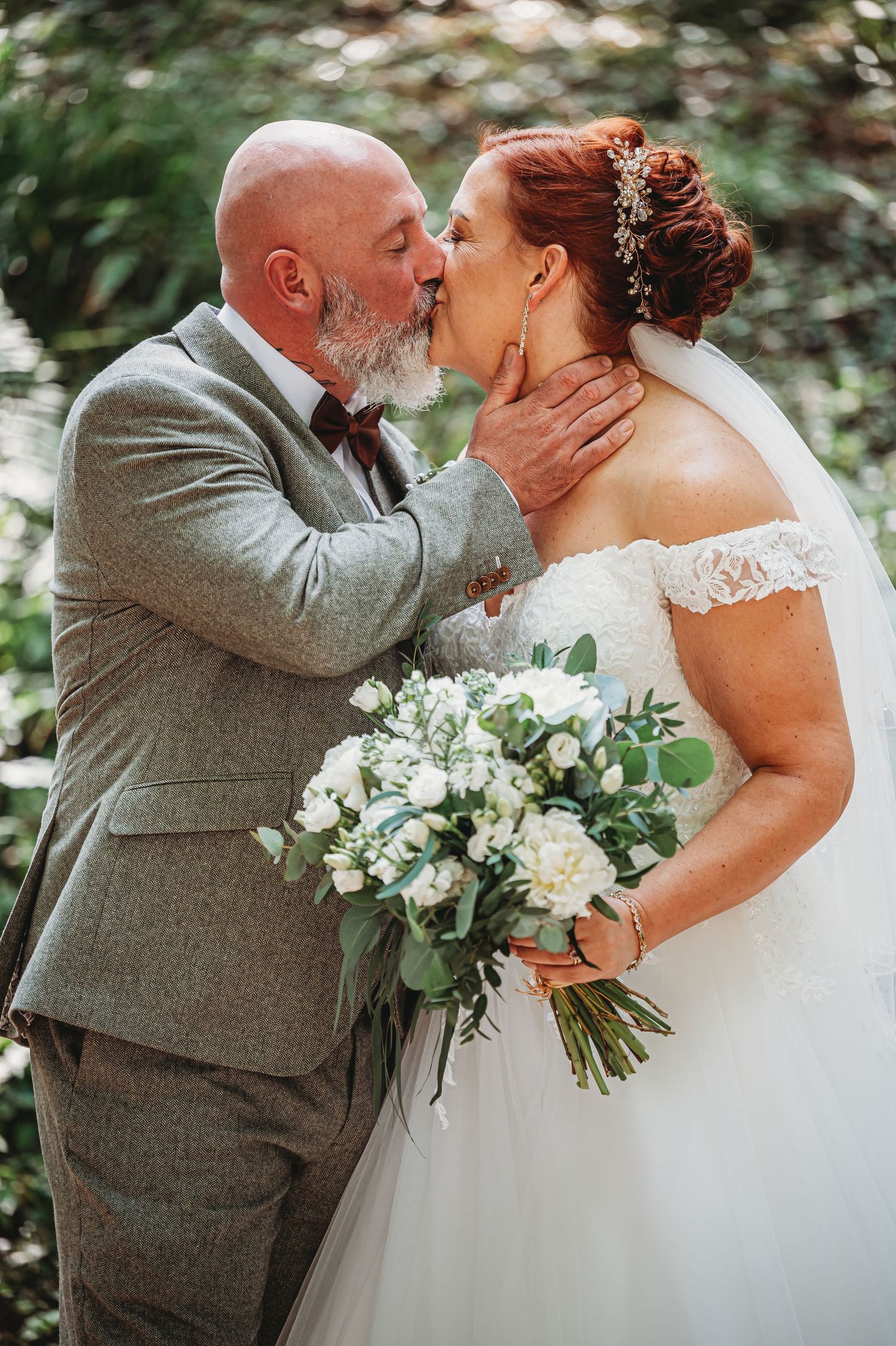A romantic wedding moment captured in a garden setting with a beautiful white bouquet of flowers and greenery.
