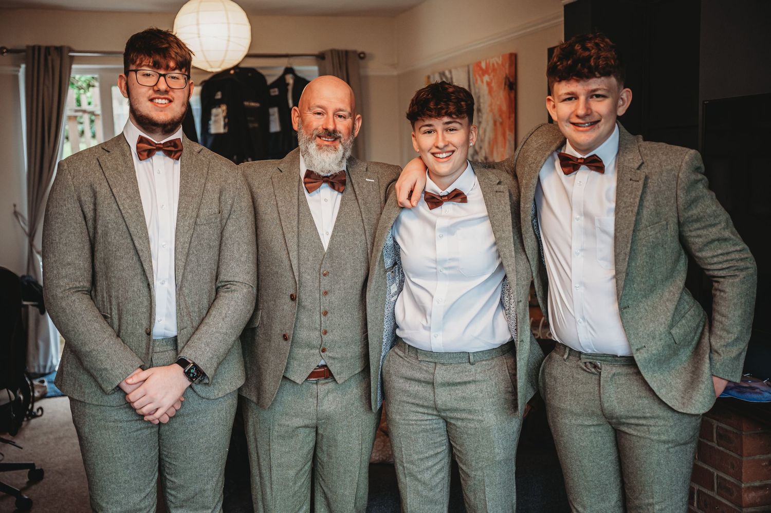 A group of four people wearing coordinated gray suits and bow ties smile together at a formal event.