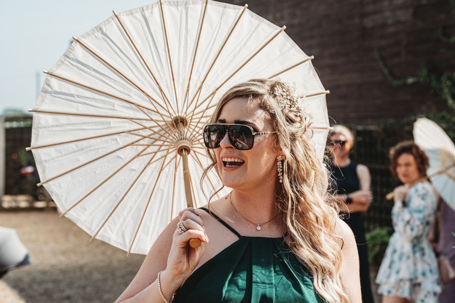 A happy festival guest holding a white paper parasol while wearing sunglasses at an outdoor summer event.